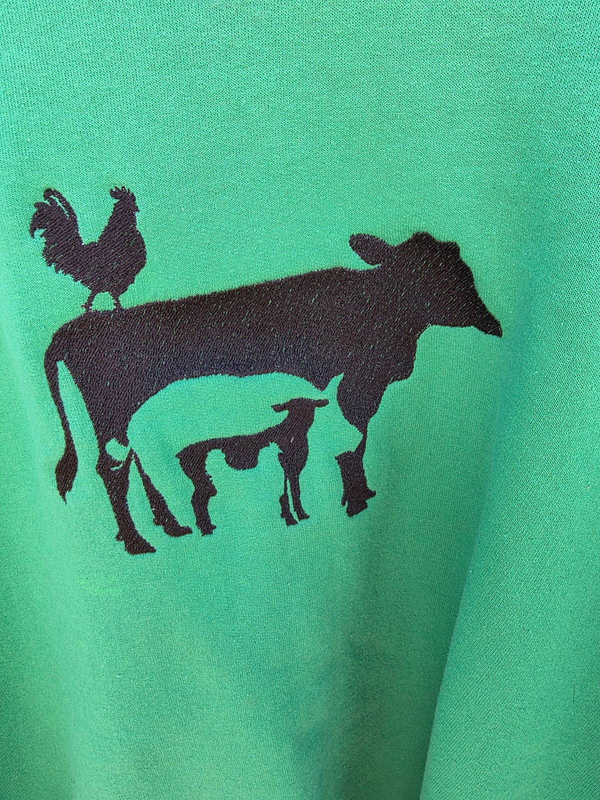 Close-up of the embroidered rooster, cow and pig design in black thread on green