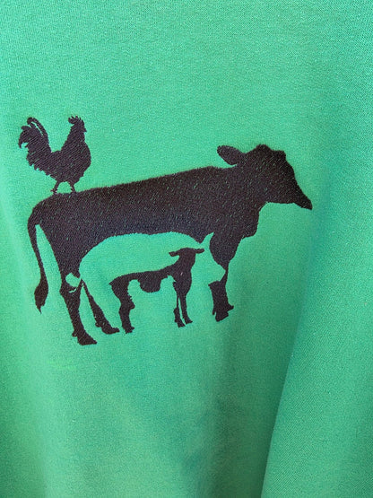 Close-up of the embroidered rooster, cow and pig design in black thread on green